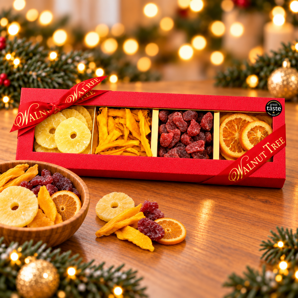 Walnut Tree luxury four-compartment dried fruit gift box featuring pineapple rings, dried mango strips, red dried fruits and orange slices, presented in red packaging with gold ribbon and Great Taste award badge against a warm festive Christmas background.