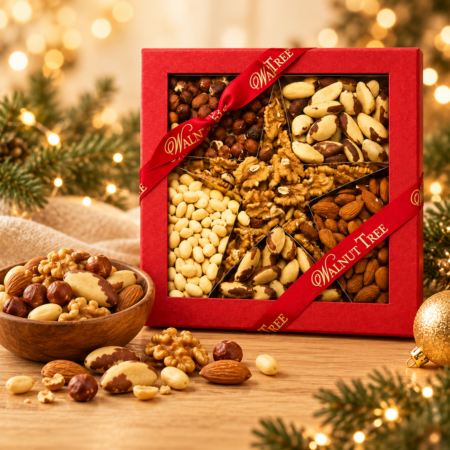 Walnut Tree luxury mixed nuts Christmas gift box featuring walnuts, almonds, hazelnuts, Brazil nuts and blanched nuts in red and gold packaging, displayed with a wooden bowl and festive golden lights.