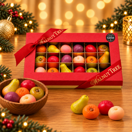 Walnut Tree luxury medium marzipan fruit gift box featuring colourful miniature marzipan apples, pears, peaches and other fruits, presented in a red gift box with gold ribbon and Great Taste award badge against a warm Christmas background.
