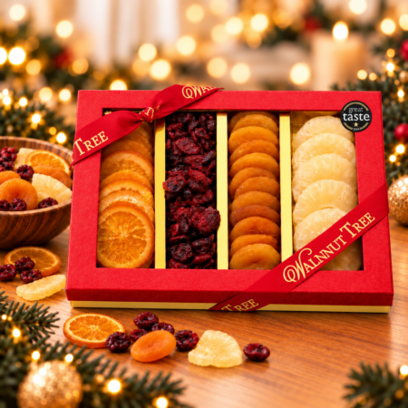 Walnut Tree luxury four-compartment dried fruit gift box featuring assorted orange slices, cranberries, apricots and pineapple, presented in red packaging with gold ribbon against a warm festive Christmas background.