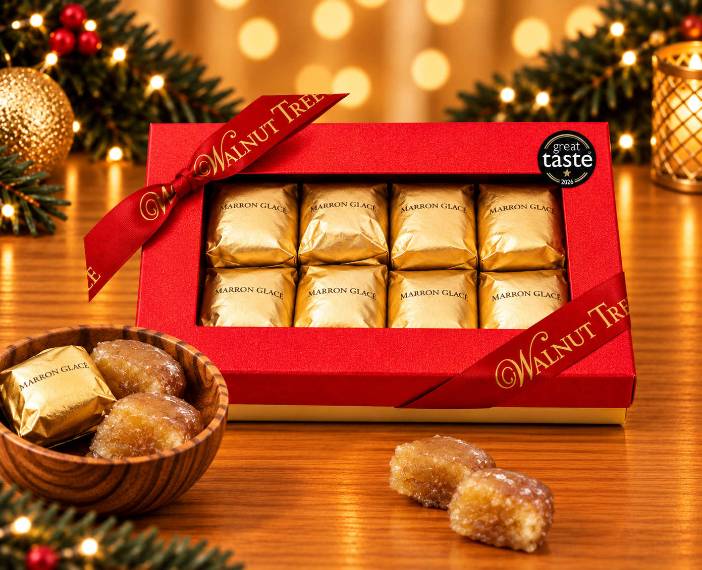 Walnut Tree luxury medium gift box containing eight individually gold-wrapped marrons glacés (candied chestnuts), finished with a red satin ribbon, gold lettering and Great Taste award badge, displayed with a wooden bowl and warm Christmas lights.