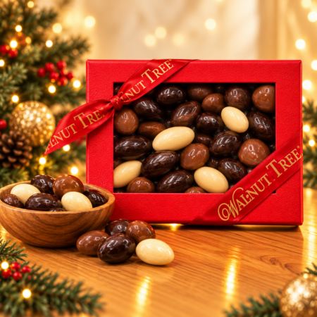 Walnut Tree luxury red rectangular Christmas gift box filled with cocoa-dusted confections, finished with a gold-lettered satin ribbon and displayed beside a wooden bowl against warm golden Christmas lights.