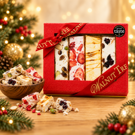 Walnut Tree luxury Christmas gift box featuring four varieties of artisan nougat with nuts, strawberries, caramel and cherries, presented in red and gold packaging with a Great Taste award, wooden bowl and warm festive lights.