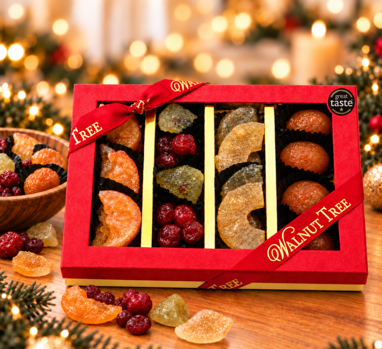 Walnut Tree luxury four-compartment glacé fruit gift box featuring assorted colourful candied fruits, presented in red packaging with gold ribbon, a wooden bowl of glacé fruits and warm festive Christmas lights.