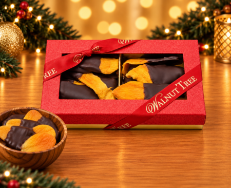 Walnut Tree luxury medium gift box featuring chocolate-dipped dried fruit, presented in red patterned packaging with gold Walnut Tree ribbon, a wooden bowl and warm golden Christmas lights.