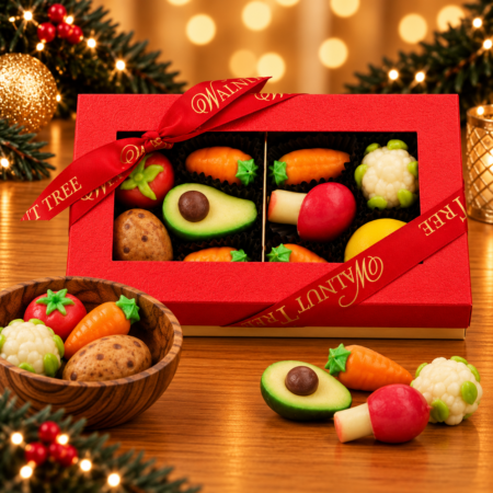 Walnut Tree luxury medium marzipan gift box featuring colourful miniature marzipan vegetables, including carrots, avocado, cauliflower and radish, presented in a red gift box with gold Walnut Tree ribbon against a warm Christmas background.