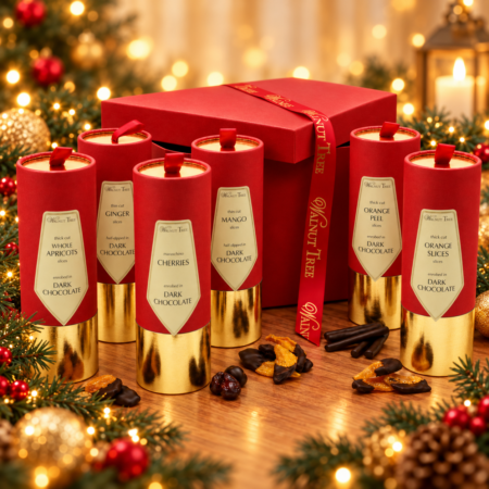 Walnut Tree mango, orange peel and ginger scrolls dipped in dark chocolate, presented in red and gold gift packaging with festive greenery on a white background.