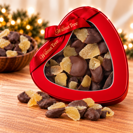 Walnut Tree dark chocolate dipped crystallised ginger in a red heart-shaped gift tin with branded ribbon, surrounded by chocolate ginger pieces in a festive Christmas setting.