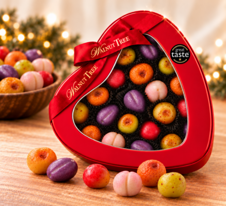 Walnut Tree luxury marzipan fruits in a red heart-shaped gift tin with branded ribbon and Great Taste award, surrounded by colourful handmade-style miniature marzipan fruits in a festive Christmas setting.